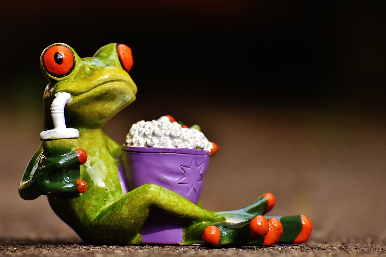 Ceramic frog reclining with popcorn and a drink, as if s/he were watching a film.