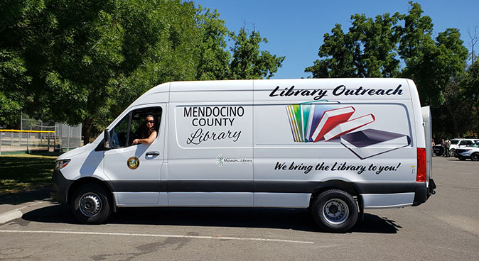 Mendocino County Library outreach van in parking lot with woman. We bring the library to you!