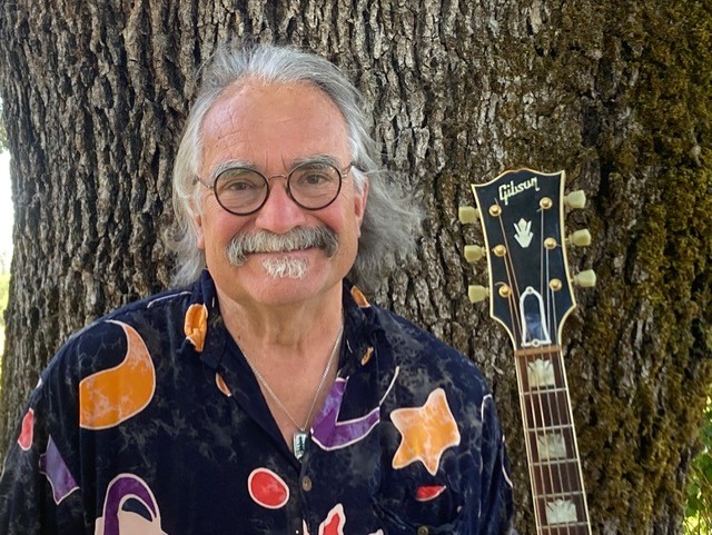 man standing in front of tree with guitar.