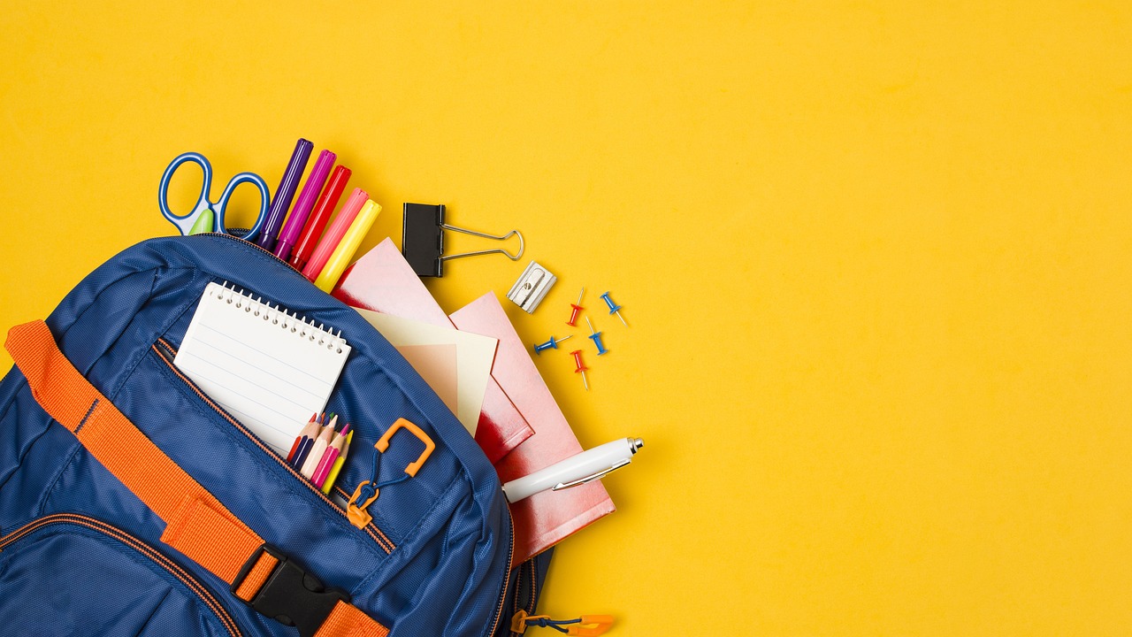 backpack with school supplies such as paper, pencils, and scissors sticking out of it.