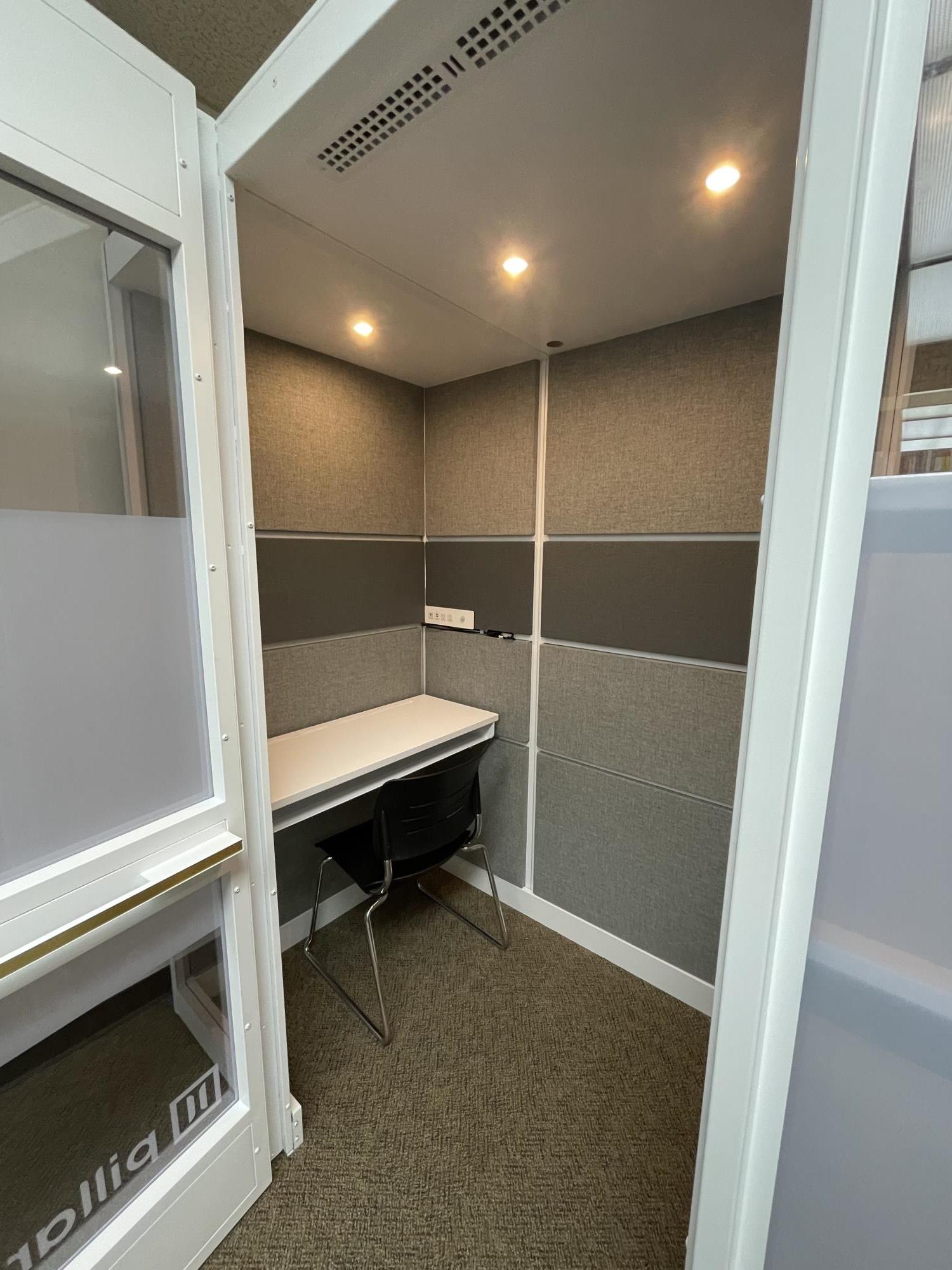 Inside view of study booth with open glass door, desk, chair, and lights.